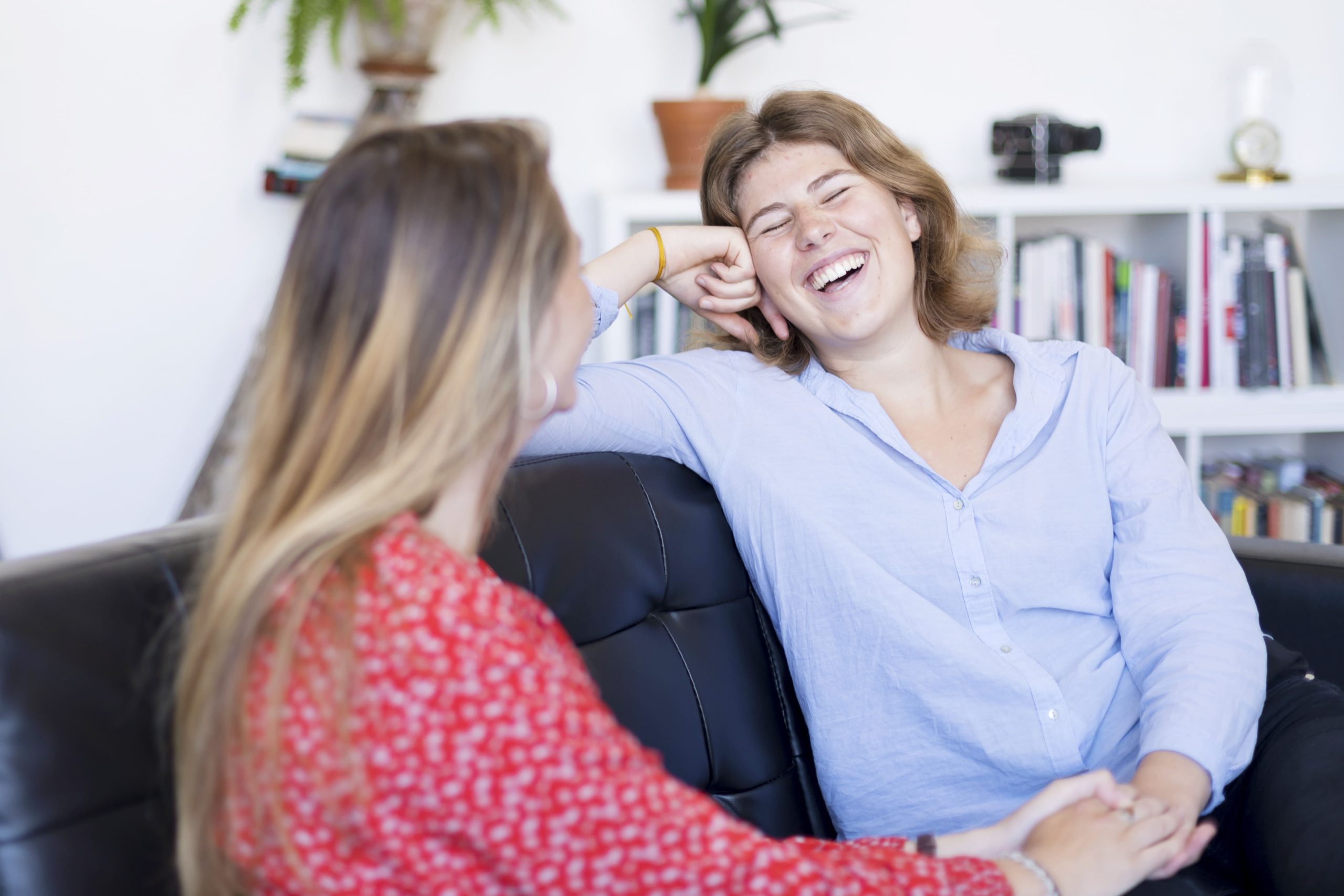 Dos mujeres jóvenes conversando y riendo sentadas en un sofá