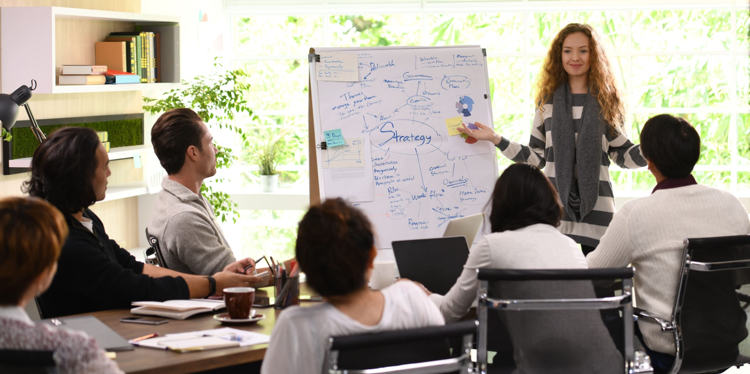 Mujer presentando una estrategia de trabajo a sus compañeros en una sala de reuniones
